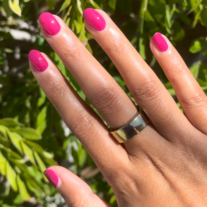 Hand with nails painted in Biggest Bow bright magenta gel polish showing vibrant at-home manicure outdoors
