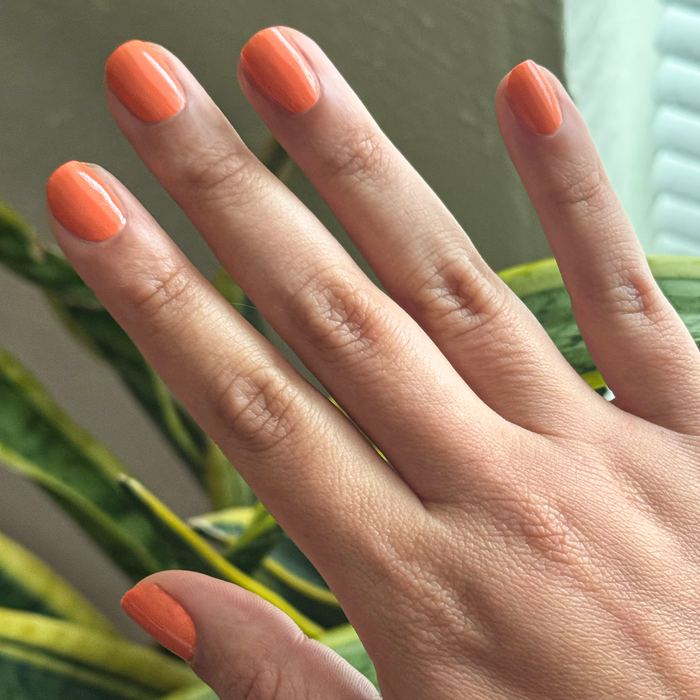 Hand with short, neatly shaped nails painted bright tangerine using Bounce Back quick-dry polish for at-home mani