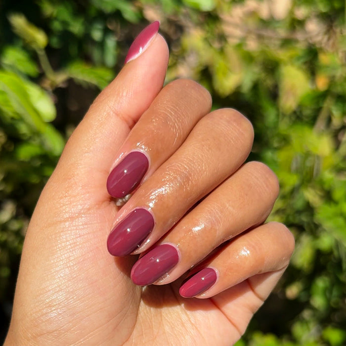 Hand with oval nails painted in Don’t Spill on the White Couch deep dusty berry red gel polish manicure outdoors