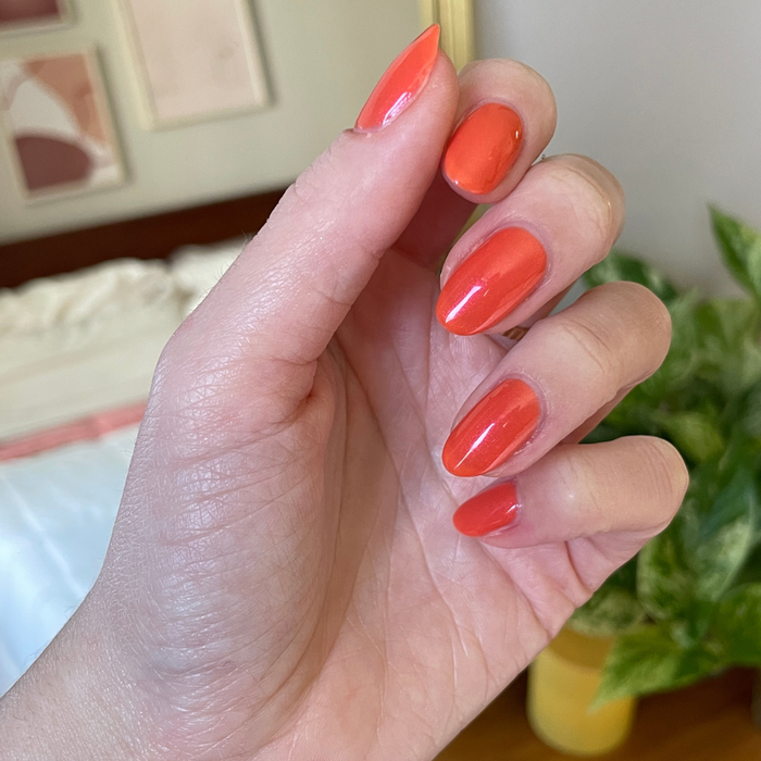 Hand with glossy nails painted in I’ll Take Another Spritz bright red-orange gel polish for an at home mani look