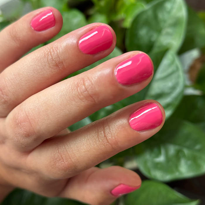 Close-up of a hand with nails painted in glossy bright hot pink Love All polish for a fresh at-home manicure