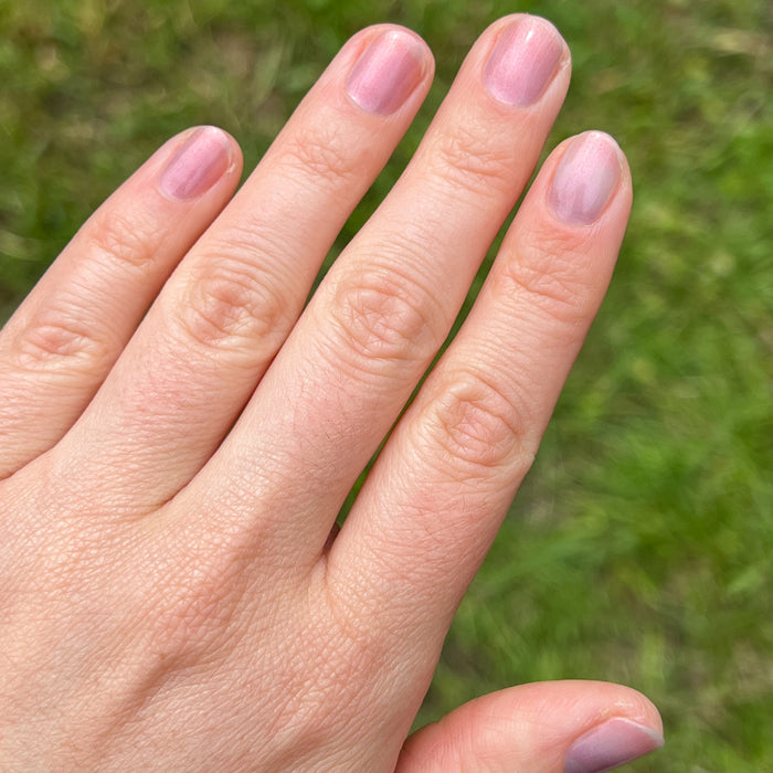Hand with natural nails showing sheer purple, pink, and gold iridescent manicure using Mermaid Hair polish outdoors