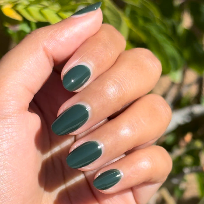 Hand with smooth polished nails in One For You, Two For Me gel polish showing dark emerald green manicure by Olive and June