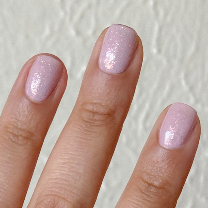 The Pixie Effect Top Coat adding a sparkling iridescent shimmer over soft pink polish for a magical manicure look
