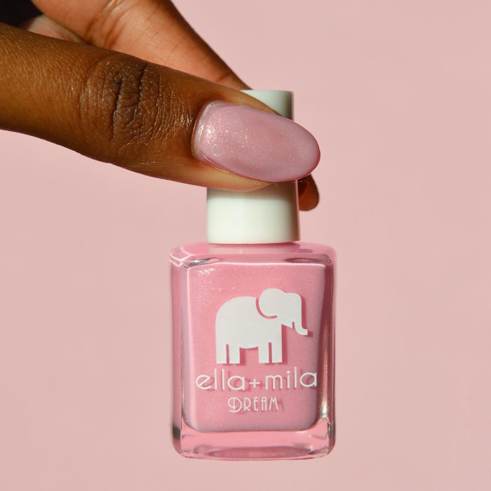 Toes Down Chin Up shimmery pink nail polish on a deep skin tone, holding the bottle on a pink background