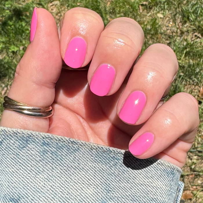 Close-up of hand with glossy bright peony pink Your Favorite Suit gel polish manicure outdoors in natural light