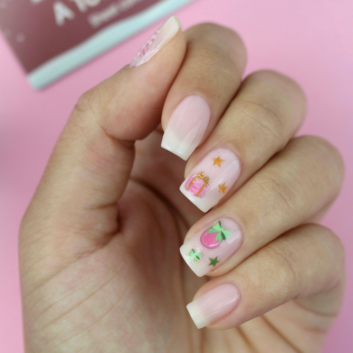A Touch of Cheer candy cane and holly decals on a sheer pink manicure with the packaging