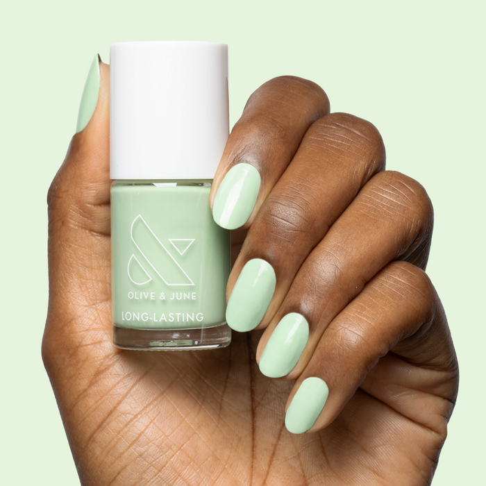 Hand holding bottle of Aced It pastel green polish with matching long-lasting manicure on nails