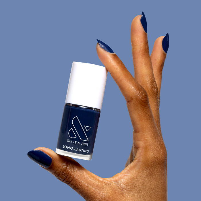 Hand with glossy navy blue gel polish holding a bottle of Ack, A Shark! long-lasting nail polish by Olive and June