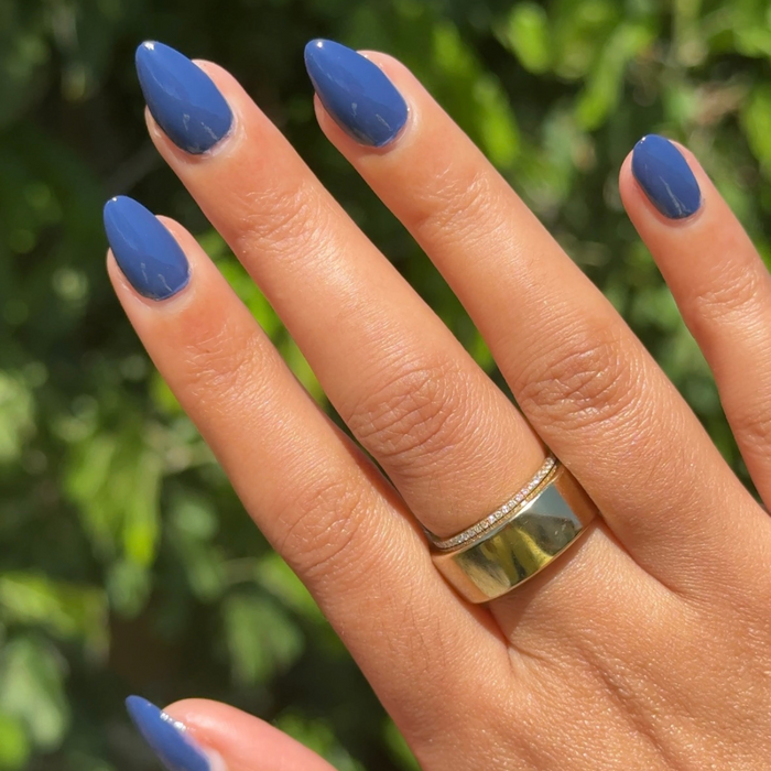 Hand with glossy navy blue nails painted with Ack, A Shark! gel polish for a sleek and durable manicure look