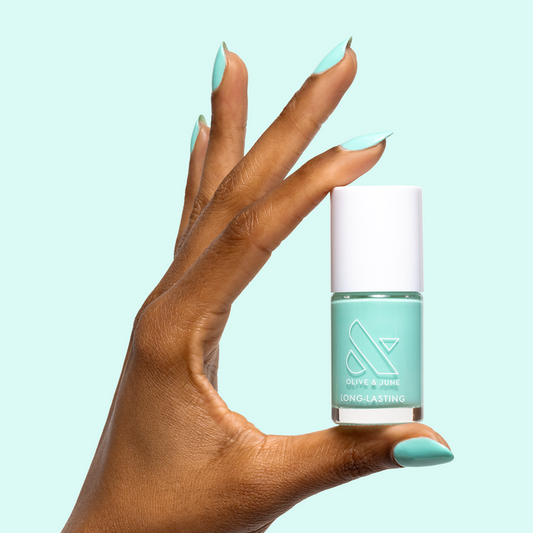Hand with smooth nails painted in All Manis on Deck bright blue-green gel polish holding matching polish bottle