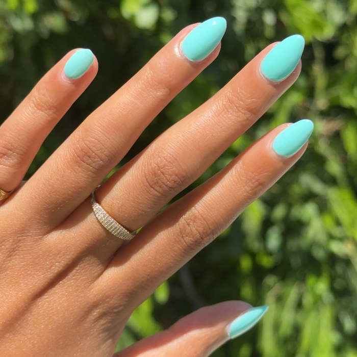 Hand with almond-shaped nails polished in All Manis on Deck bright blue-green gel polish in natural outdoor light