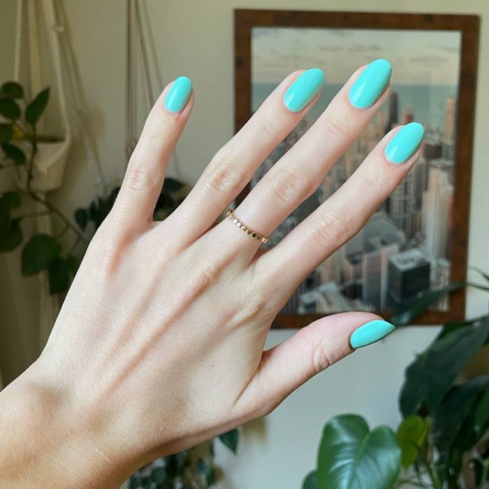 Hand with nails painted in bright All Manis on Deck blue-green gel polish showing polished manicure indoors