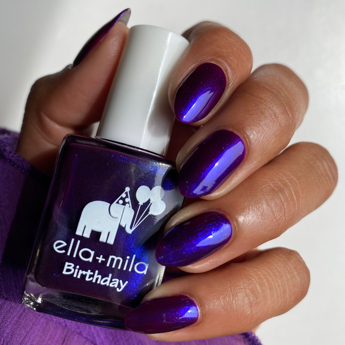 Amethyst Kiss iridescent purple blue nail polish on a medium skin tone, hand holding the bottle