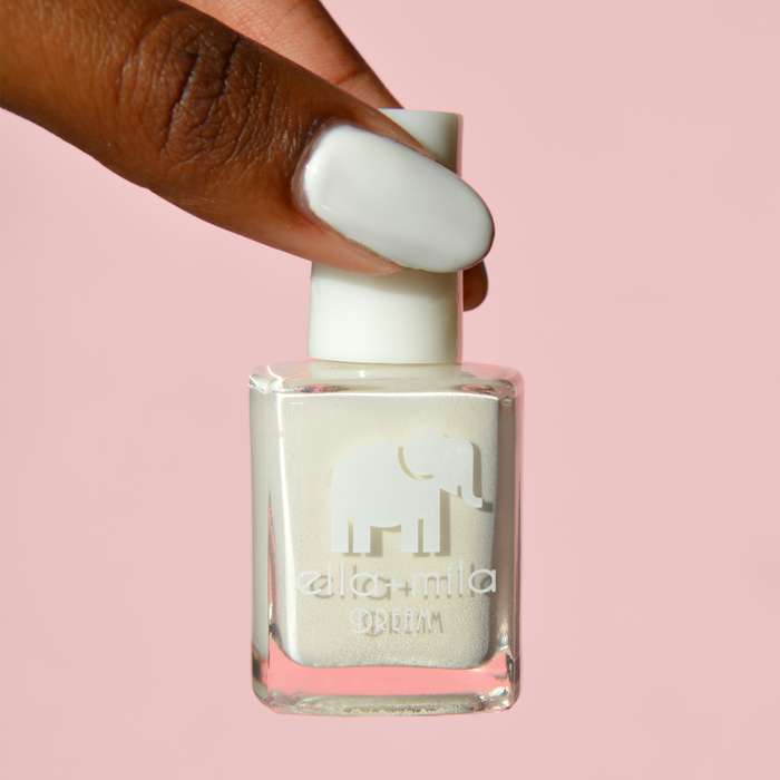 Ballet It On Me milky ivory nail polish on a deep skin tone, holding the bottle on a pink background