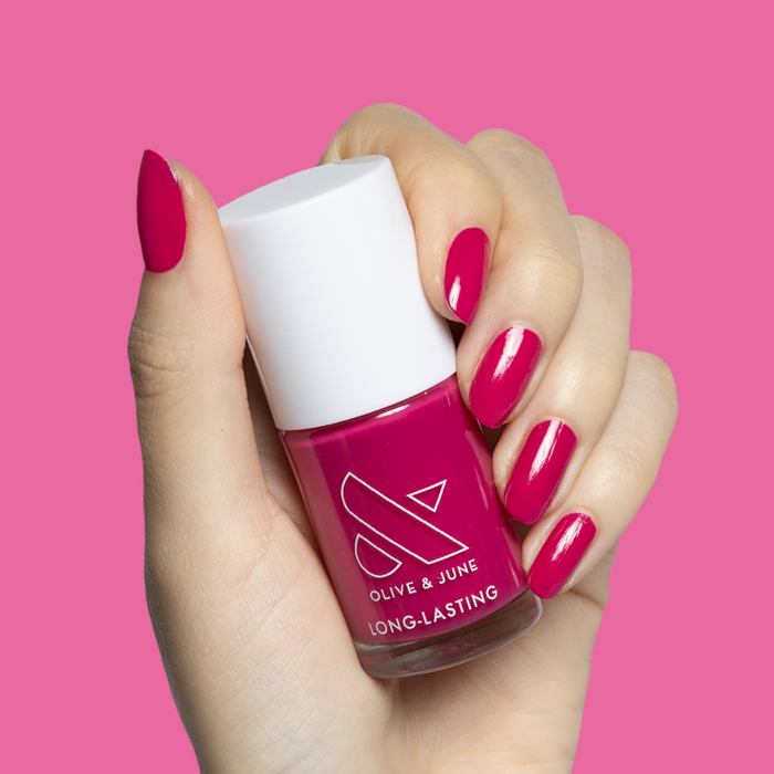 Hand with glossy nails painted in Biggest Bow magenta pink gel polish holding Olive and June bottle