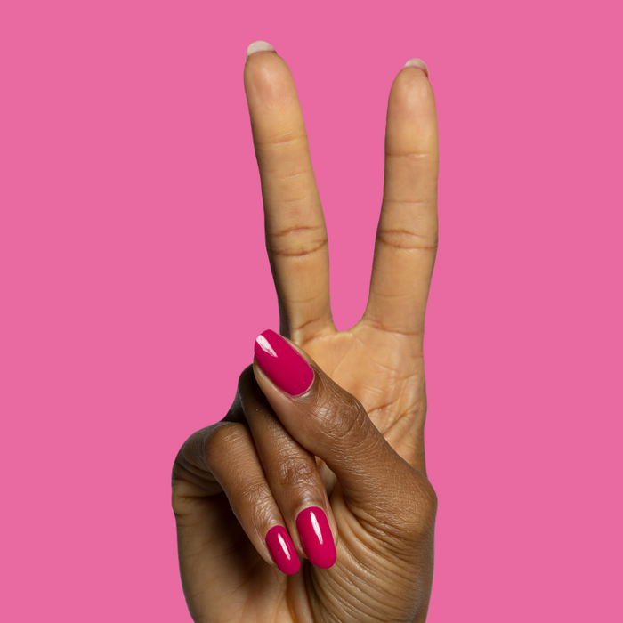 Hand with glossy magenta pink nails painted in Biggest Bow gel polish showing vibrant mani on pink background
