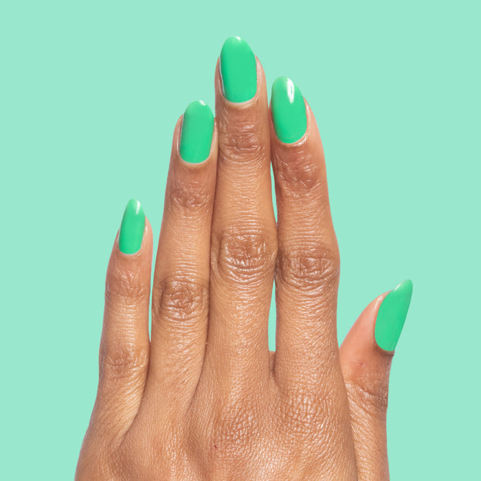 Hand with neatly manicured nails painted in Bocce Ball green polish on a matching green background