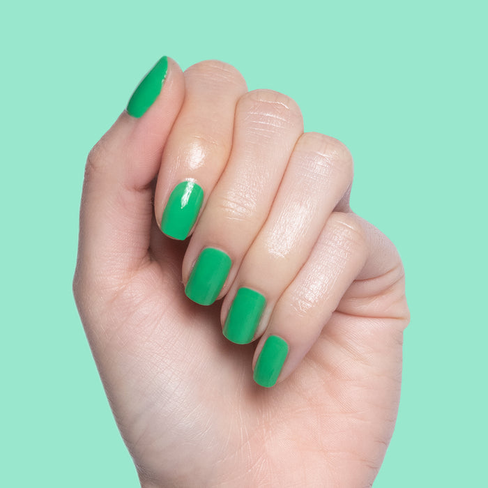 Hand with smooth nails painted in vibrant Bocce Ball green polish on a soft mint background