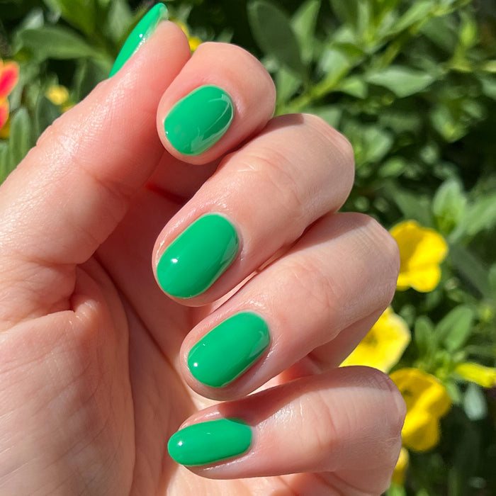 Hand with glossy Bocce Ball green manicure in natural sunlight with blurred garden flowers in the background