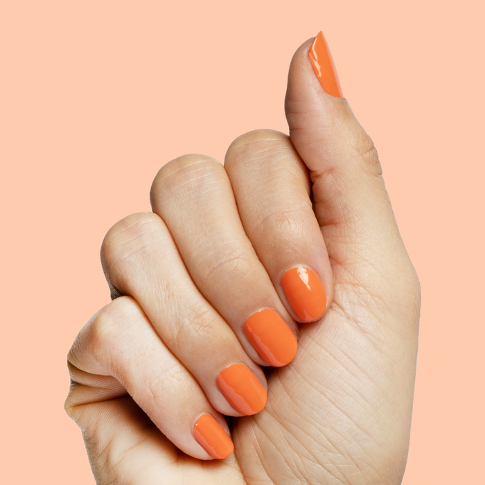Hand with short nails painted bright tangerine using Bounce Back nail polish for a fresh at-home mani