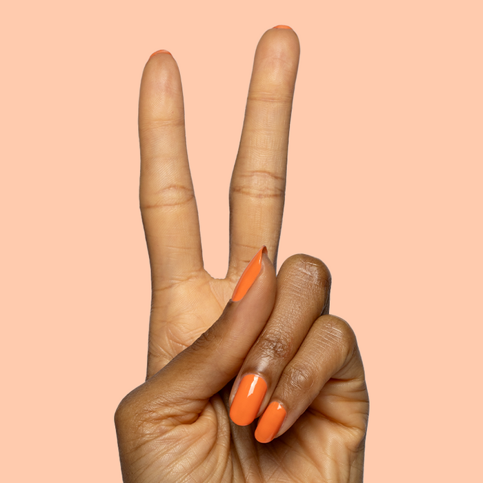 Hand with glossy nails painted vibrant orange using Bounce Back polish by Olive and June showing peace sign