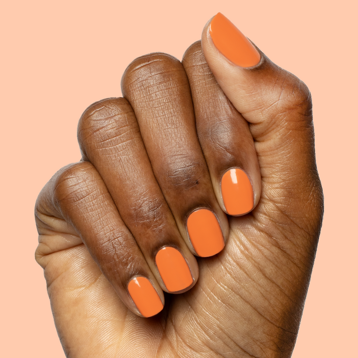 Hand with rounded nails painted bright tangerine using Bounce Back polish for a glossy at-home manicure