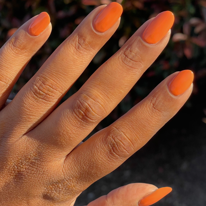 Hand with medium-length nails painted bright orange using Bounce Back polish for a glossy at-home manicure