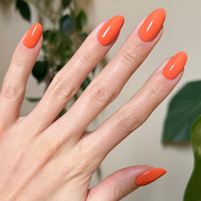 Hand with almond-shaped nails painted bright tangerine orange using Bounce Back quick-dry polish for a polished mani