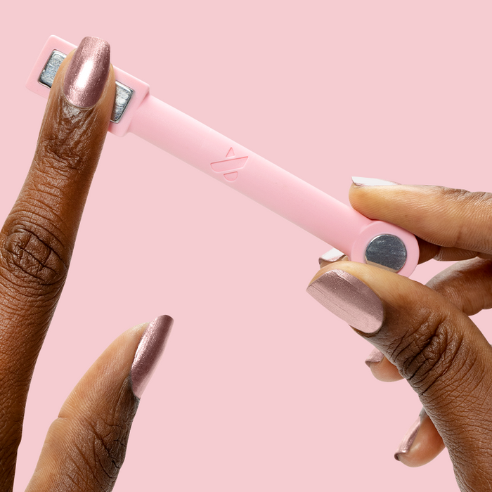 Hand holding Bronze Velvet magnetic polish on nails using pink magnetic tool for a shimmering mani effect