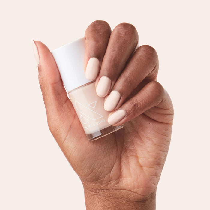 Dark-skinned hand holding Cable Knit bottle with nails polished in creamy peach neutral gel polish shade