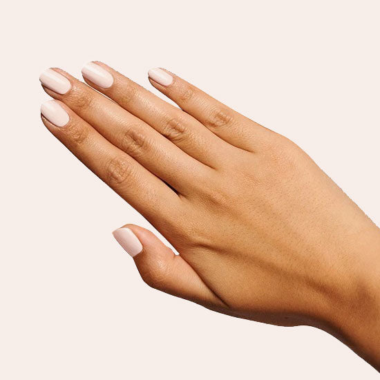 Hand with nails polished in creamy peach shade Cable Knit gel polish against soft beige background for mani