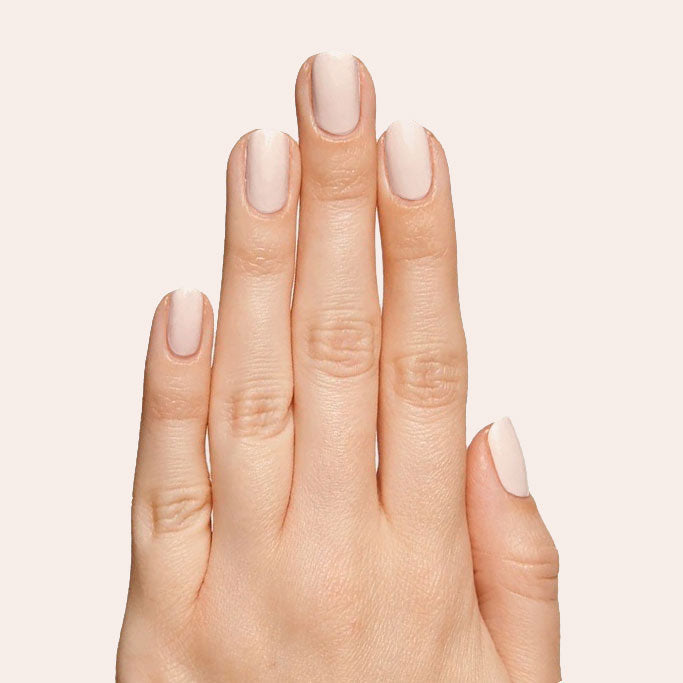 Hand with nails coated in Cable Knit creamy peach neutral gel polish against soft pale background for mani