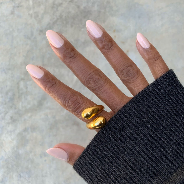 Hand with nails painted in creamy peach Cable Knit gel polish wearing gold rings and cozy black sweater sleeve for mani