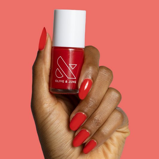 Hand holding bottle of Candy Dipped nail polish with nails painted in bright red for vibrant at-home manicure