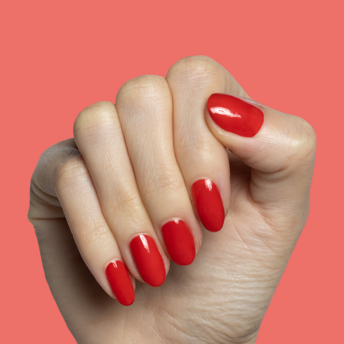 Hand with glossy nails painted in Candy Dipped red polish showing a bright at-home manicure by Olive and June