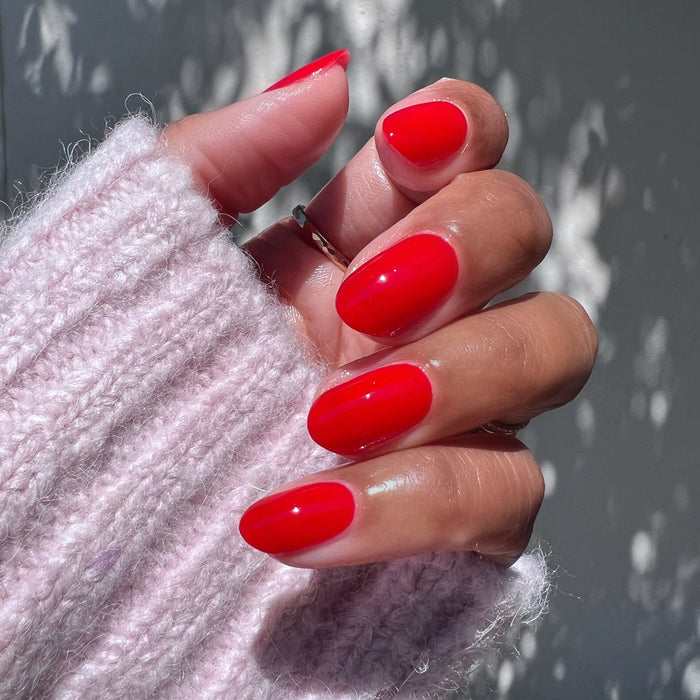 Hand with nails coated in glossy Candy Dipped red gel polish showing a polished at-home mani by Olive and June