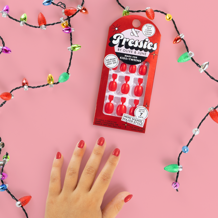 Cherry Chrome Sleigh - Pressies | Extra Short Short | Round bright red press-on nails shown on hand with holiday lights on pink background