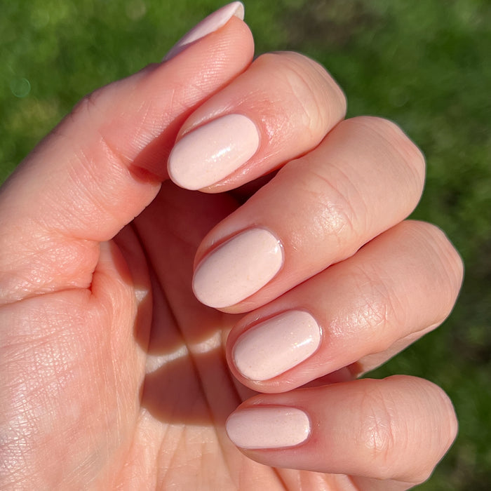 Hand with short rounded nails painted in shimmery neutral beige using cold foam pls nail polish for a natural mani