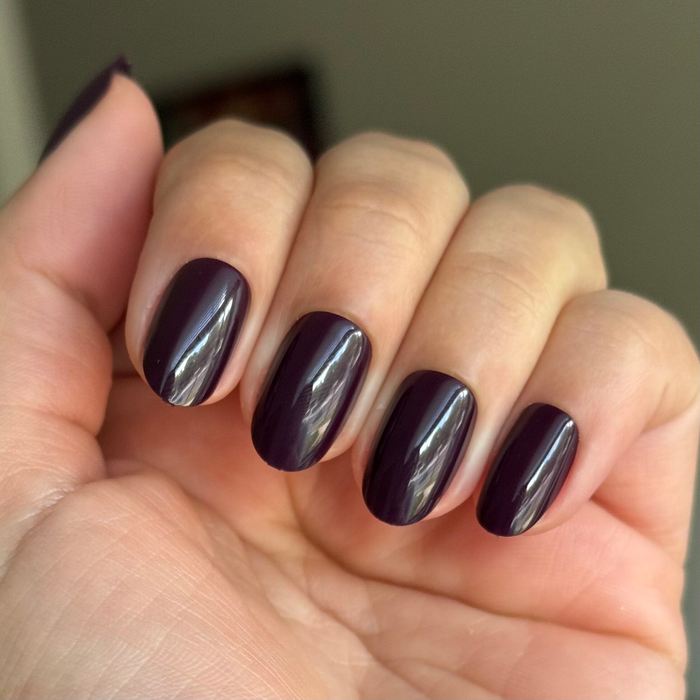 Hand with fair skin wearing glossy Covet - Press-On | Short | Round nails in a dark plum shade with a rounded shape