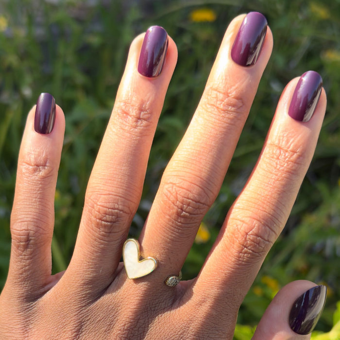 Hand with dark skin tone wearing glossy Covet - Press-On | Short | Round nails in a cool deep plum shade outdoors