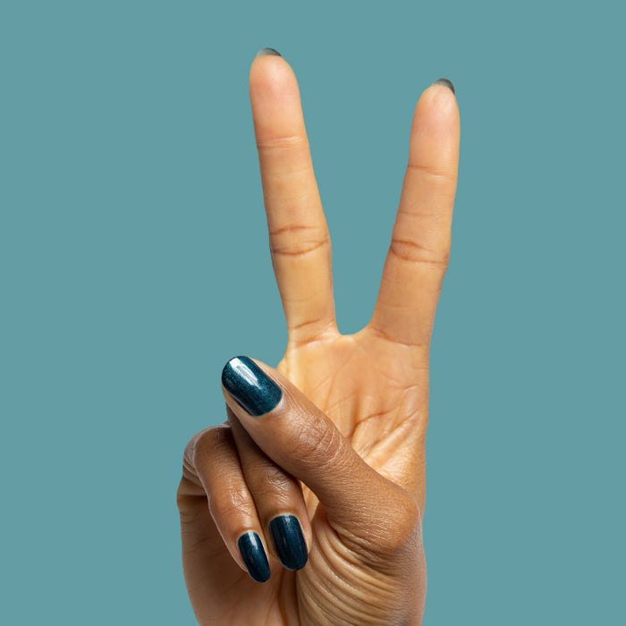 Hand showing two fingers with nails painted in deep emerald Dancing Green polish against muted blue background