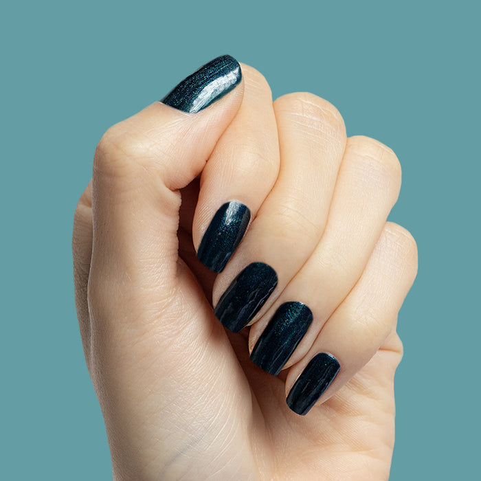Hand with medium-length nails painted in deep emerald chrome shade Dancing Green against teal background