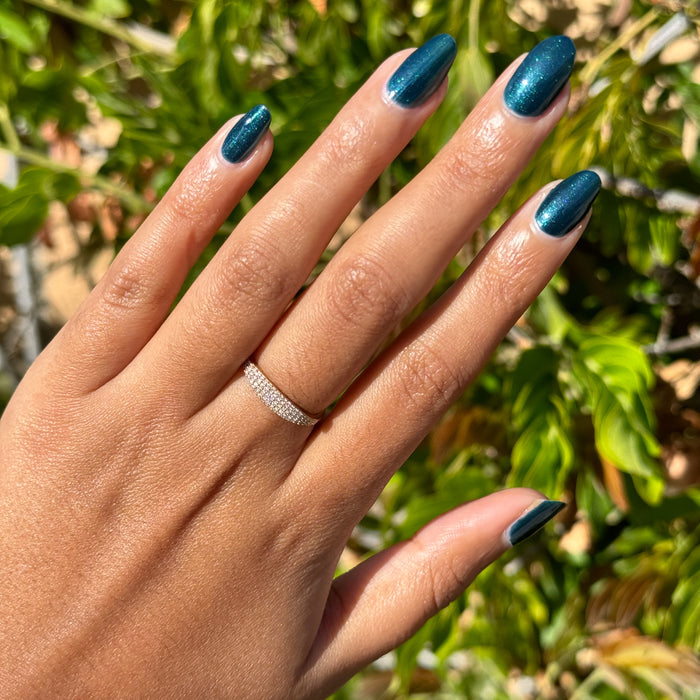 Hand with medium-length nails painted in shimmering deep Dancing Green polish wearing a delicate ring outdoors