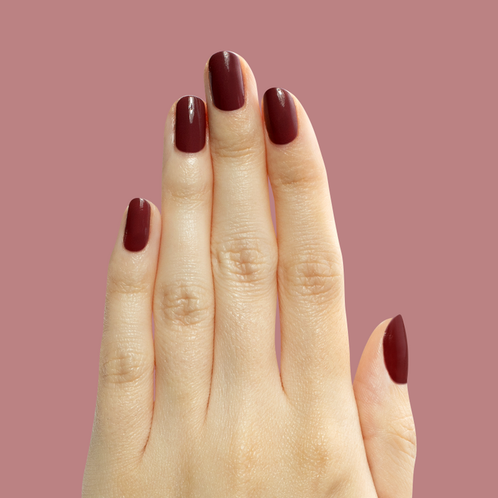 Hand with medium-length nails polished in Don’t Spill on the White Couch deep berry red gel polish manicure