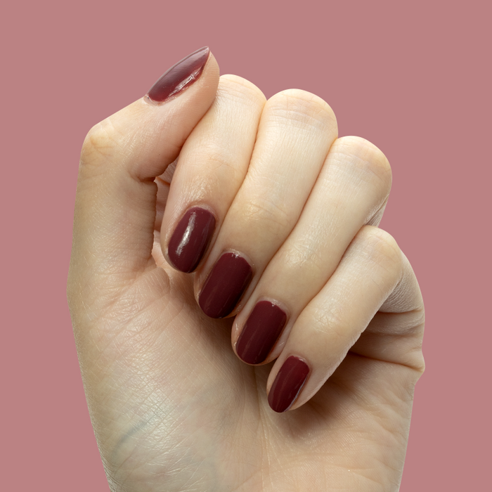Hand with short nails painted in Don’t Spill on the White Couch deep dusty berry red gel polish manicure