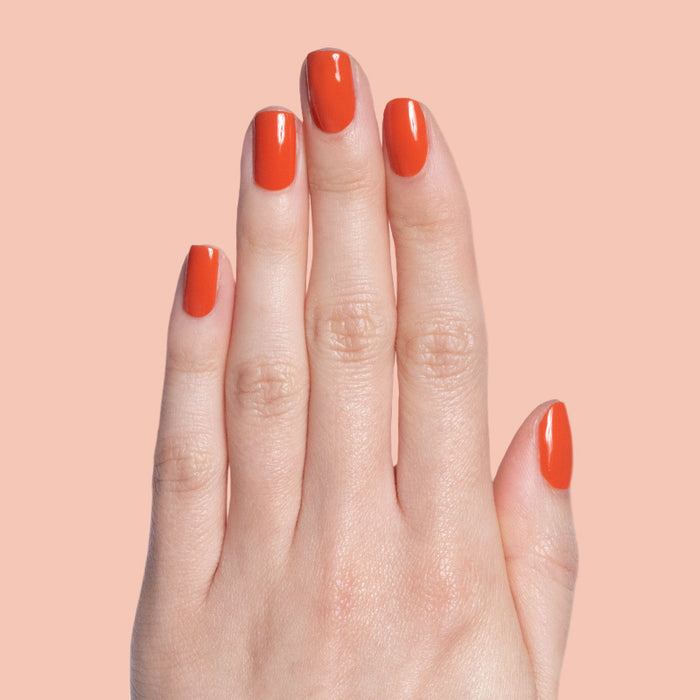 Hand with glossy nails painted in vibrant burnt orange Flowerpot polish on a soft peach background