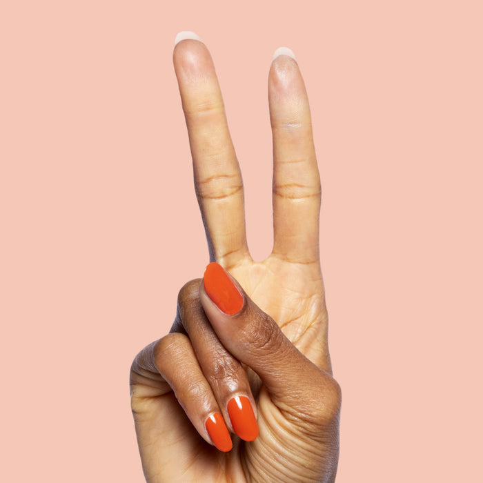 Hand with glossy nails in burnt orange Flowerpot polish forming peace sign on soft peach background
