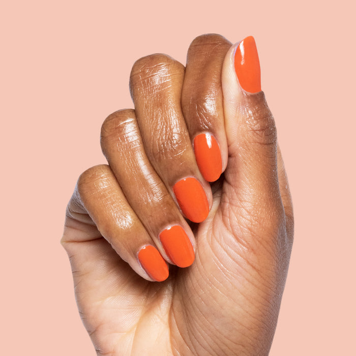 Hand with smooth nails painted in glossy Flowerpot burnt orange polish on a soft peach background