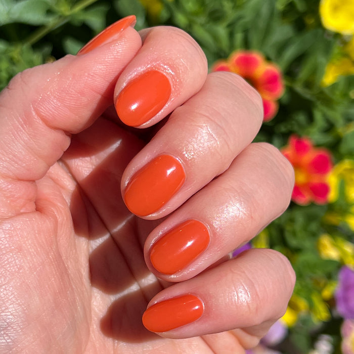 Hand with glossy nails painted in bright Flowerpot polish against colorful garden flowers for a summer manicure